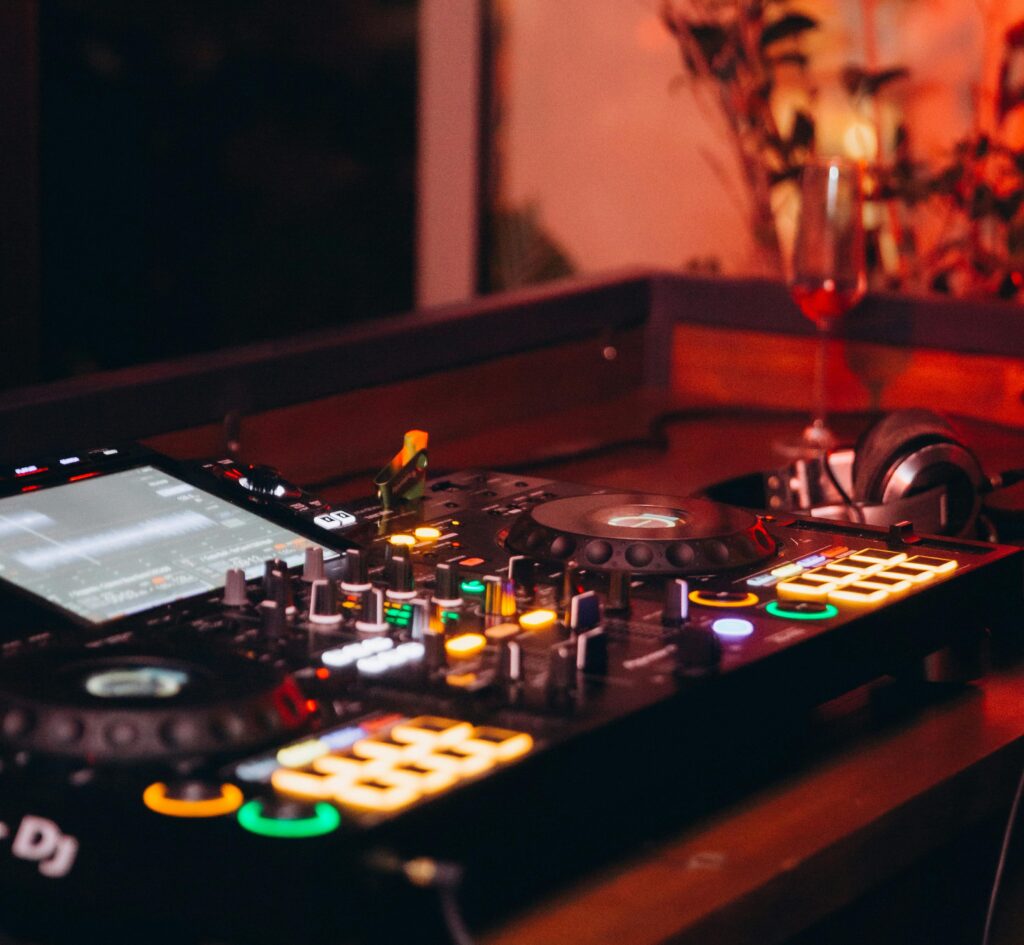 Colorful DJ mixer and headphones on a wooden table in a dimly lit nightclub, exuding a lively atmosphere.